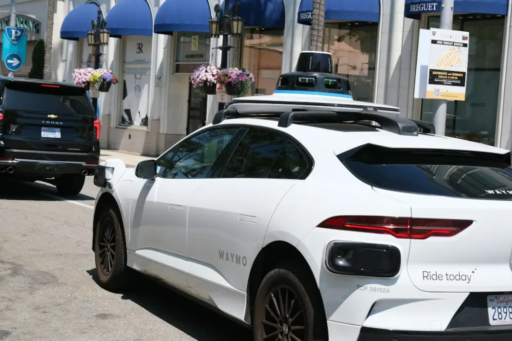 A white Waymo autonomous vehicle with roof sensors parked on a city street, illustrating engineering coherent mobility